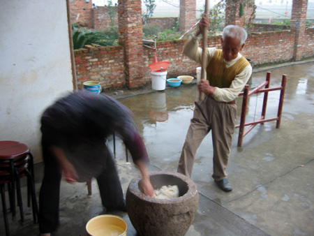 夫妻二人一个挥动木椿，一个翻着麻糍，动作麻利，行如流水。